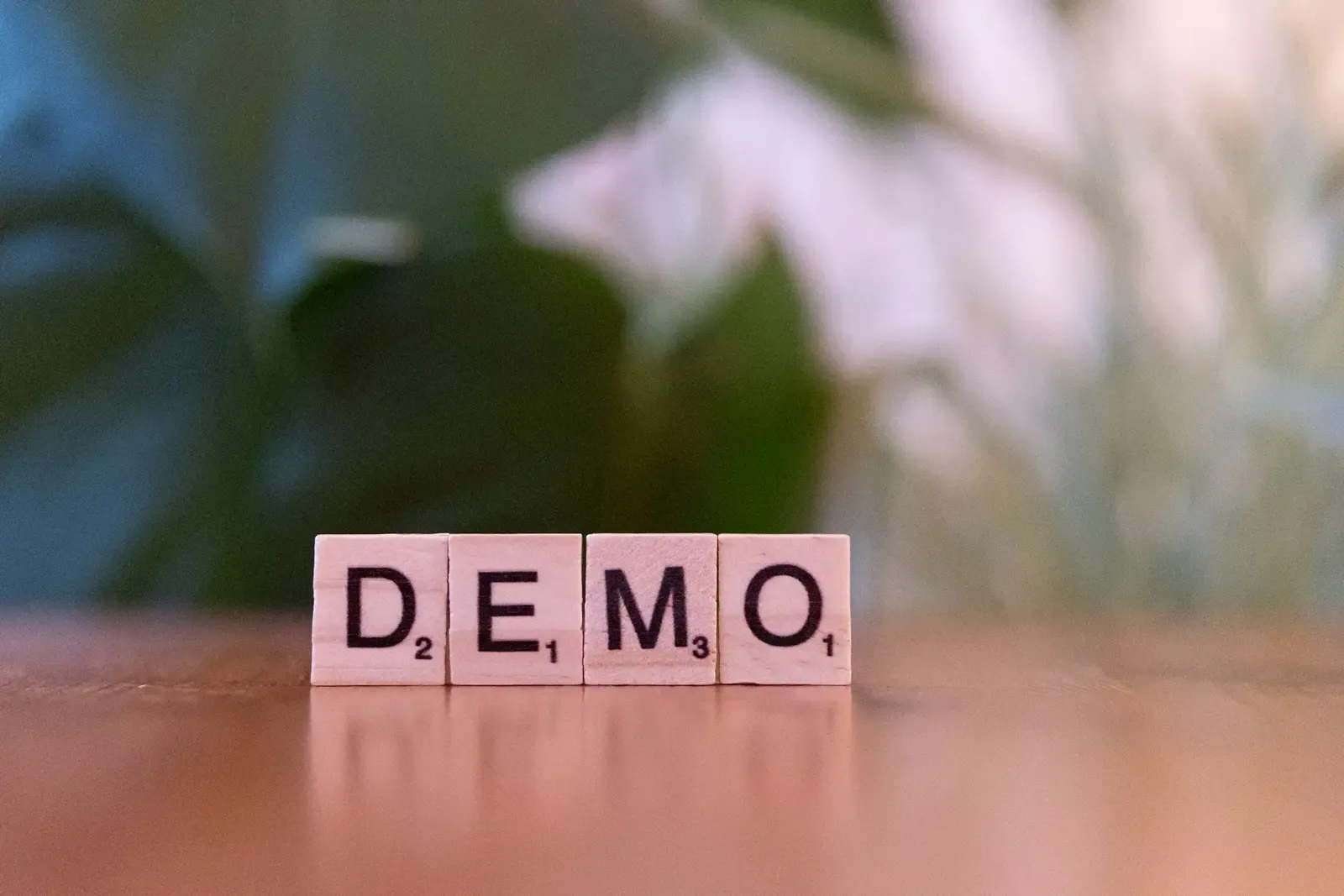 Drewniane płytki do scrabble ułożone w słowo DEMO na blacie, w tle rozmyta zieleń